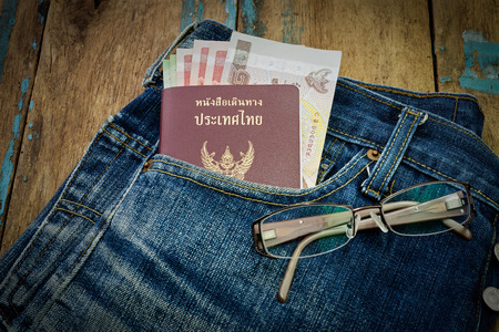 Passport and money on jeans and eyeglasses, on floor woodenの写真素材