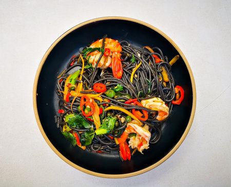 Black spaghetti with prawns and vegetables in a black plate.の写真素材