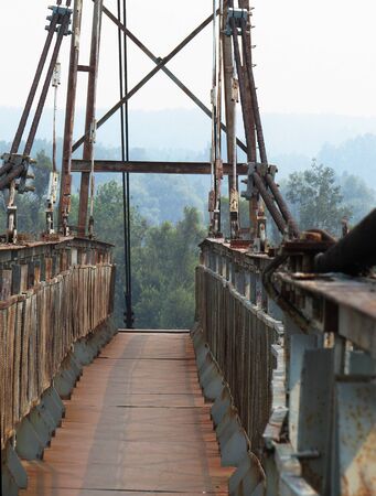 Photograph of a small metal iron bridge with wooden planks and metal handrails, with a background in the form of a misty blue forest.の写真素材