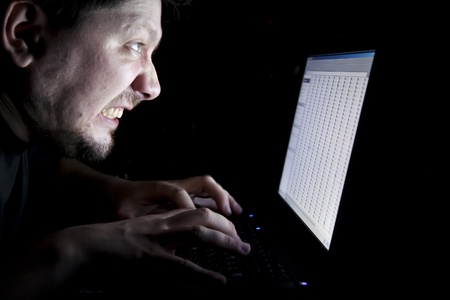 angry man working on laptop in the dark