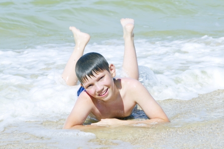 Boy lying on sand beach in the surf at sunny dayの写真素材