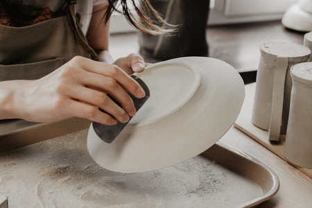 Woman making pottery. Close-up of process of sanding clay plateの写真素材