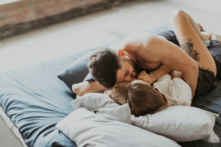 beautiful loving couple kisses and cuddles in bedの写真素材