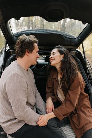 Young beautiful couple relaxing together sitting on a car trunkの写真素材