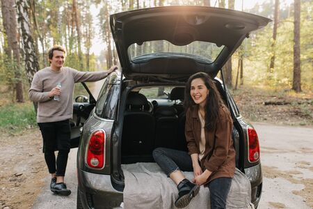 Young beautiful couple relaxing together sitting on a car trunkの写真素材