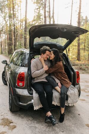 Young beautiful couple relaxing together sitting on a car trunkの写真素材