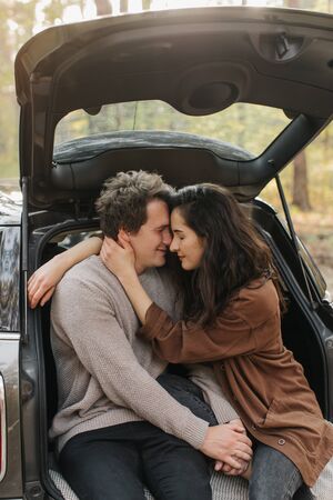 Young beautiful couple relaxing together sitting on a car trunk