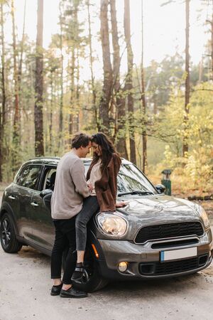 beautiful young couple in love kisses and hugs sitting on a carの写真素材