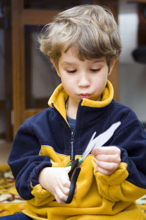 The boy scissors a slice of a white paper