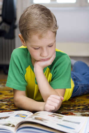 The boy reads the book lying on a floor