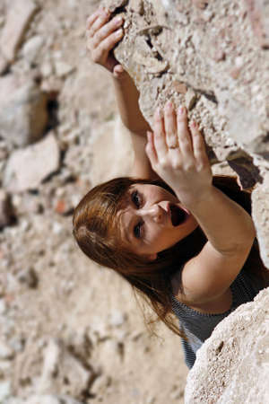 The girl hangs on the brink of a rock and asks about the helpの写真素材