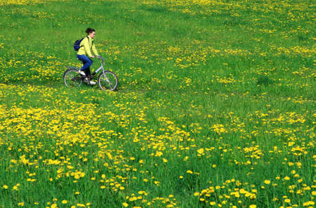 The girl rides a bike across the field on which dandelions growの写真素材