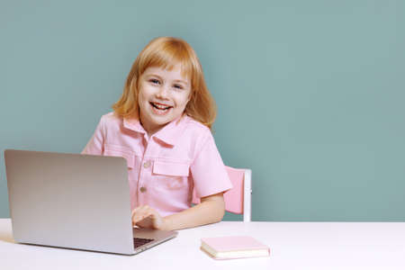 A smiling girl in pink sits at her laptop on a blue background.の写真素材