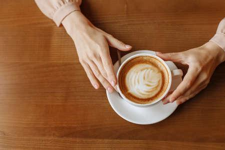 A woman holds a white cup of coffee with hands on a wooden background. view from above.の写真素材
