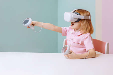 A little girl sits in virtual reality glasses and points up.