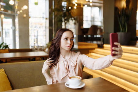 A beautiful young girl takes a selfie in a cafe.