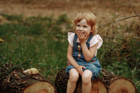 Charming little girl laughs and wonders looking at a big snail.の写真素材