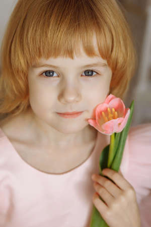 A girl in a pink dress holds a pink tulip in her hands.の写真素材