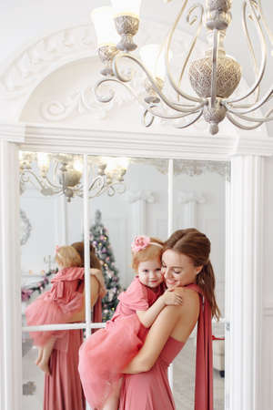 Mother and daughter in soft pink dresses near the decorated Christmas tree.の写真素材