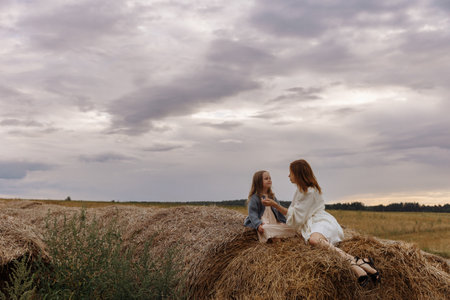 Mom and daughter are sitting on haystacksの写真素材