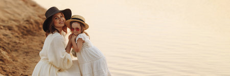 Happy mother and cute daughter are standing on the sandy shore.