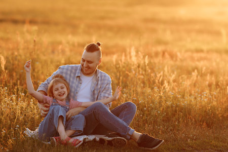 Father and daughter in the summer in the field sit on the grassの写真素材