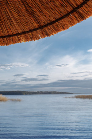 The roof of a straw umbrella against the background of blue waterの写真素材
