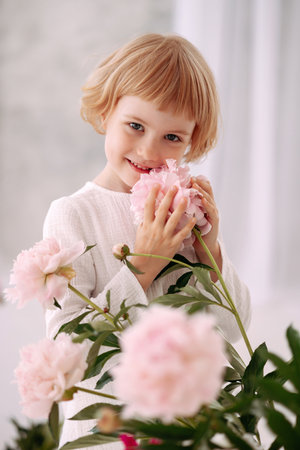 Girl 6-7 years old in a white dress holds a flowerの写真素材