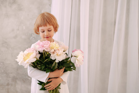 Girl 6-7 years old in a white dress holds a flowerの写真素材