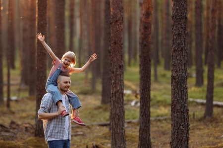 Dad and his daughter are walking along a forest road among tall pines.の写真素材