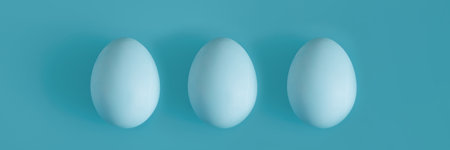Three White chicken eggs on a blue background in the center.の写真素材