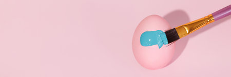 The brush paints with blue gouache a pink Easter eggの写真素材