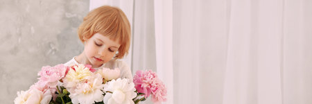 Girl 6-7 years old in a white dress holds a flowerの写真素材