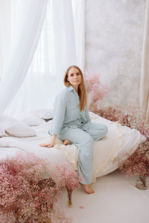 A woman in a white bathrobe sits on a bed with flowersの写真素材