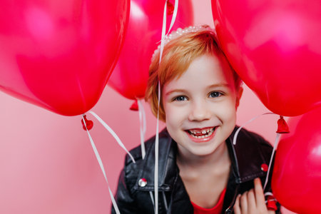 Stylish Child smiles toothlessly, wears a black leather jacket and carries balloonsの写真素材