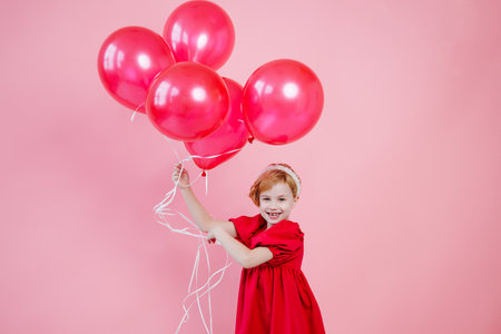 Child girl smiles toothlessly, wears a bright pink dress and carries balloonsの写真素材