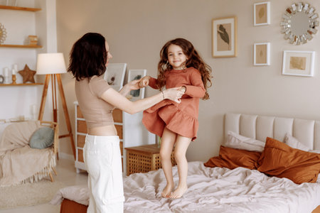 Happy mom and daughter jumping on the bedの写真素材