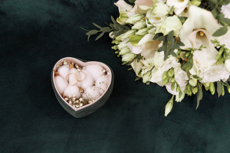Box with rings in the shape of a heart and a wedding bouquet of roses on a green background