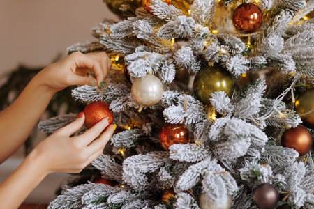 Hands decorating christmas tree with stylish bauble in atmospheric festive room.の写真素材