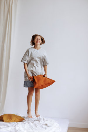 A child in casual clothes jumping on a bed with a pillow in his handsの写真素材