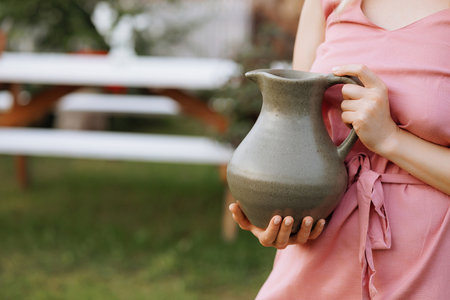 Woman holding a ceramic jug outdoors.の写真素材