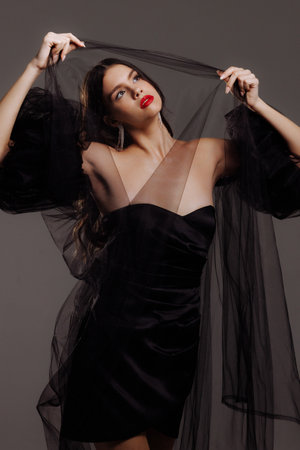 A girl in a black dress holds a black veil over her head.の写真素材