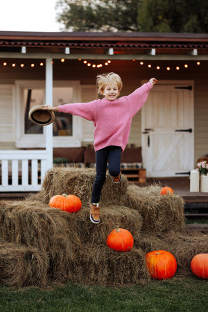 A young girl on hay bales in front of pumpkins.の写真素材