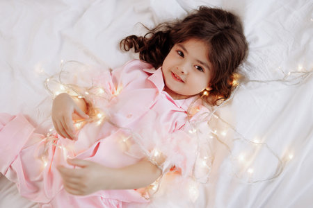 A young girl is laying on a bed with a string of lights around her