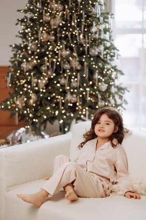 A young girl is sitting on a couch in front of a Christmas treeの写真素材