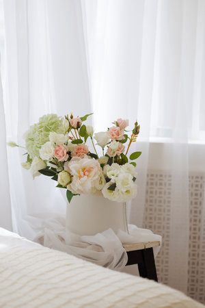 A white vase with pink flowers sits on a wooden stoolの写真素材