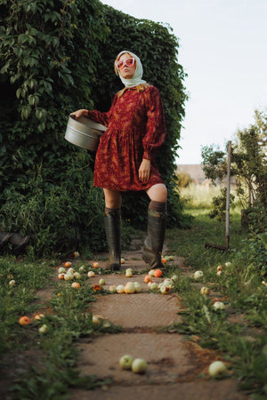 A fashionable woman in a red dress is holding a bucket full of applesの写真素材