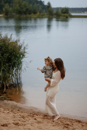Woman and child walking along peaceful lakeside beachの写真素材