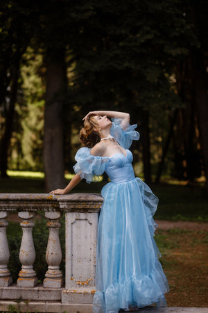 Romantic Woman in a Light Blue Gown Posing on a stone balustrade in a picturesque garden.の写真素材