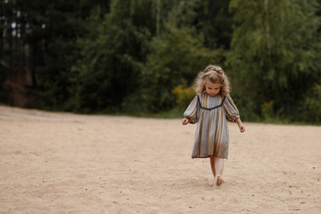 A young girl in a dress walks along a sandy beach.の写真素材